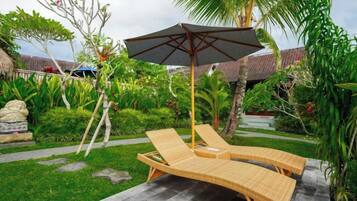 A garden with a lounge chair and umbrella, surrounded by greenery and a stone pathway.