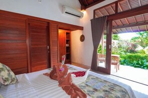 A room with a bed, wooden wardrobe, and a view of a garden. - Green Coconut Cottage Ubud (Bali)