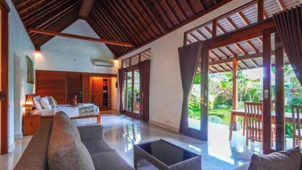 A spacious living area with a sofa, a coffee table, and a bed with a nightstand. - Green Coconut Cottage Ubud (Bali)