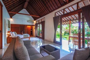 A spacious living area with a sofa, a coffee table, and a bed with a nightstand. - Green Coconut Cottage Ubud (Bali)