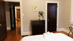 Een slaapkamer met een bed, een dressoir, een plant en een schilderij aan de muur.