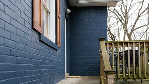 Een blauw huis met een houten voordeur, een trap van hout en een terras met stoelen.