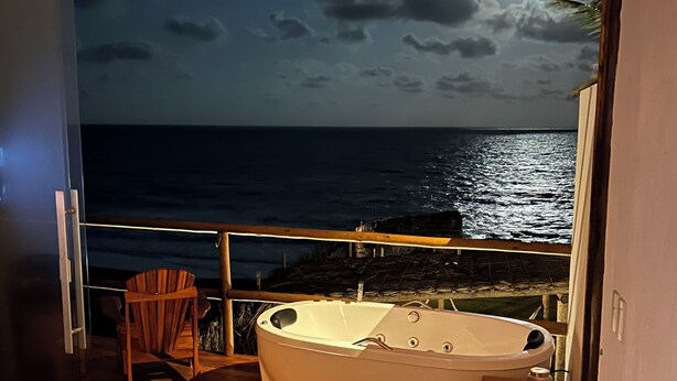 A balcony with a wooden floor, a wooden chair, and a white bathtub. - Pousada Mar no Olhar (Rio do Fogo)