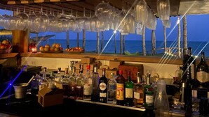 A bar with a view of the ocean, bottles of alcohol, and hanging wine glasses. - Pousada Mar no Olhar (Rio do Fogo)