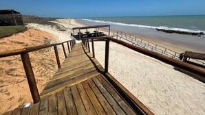 A wooden boardwalk leading to a beach with a thatched-roof structure and outdoor seating. - Pousada Mar no Olhar (Rio do Fogo)
