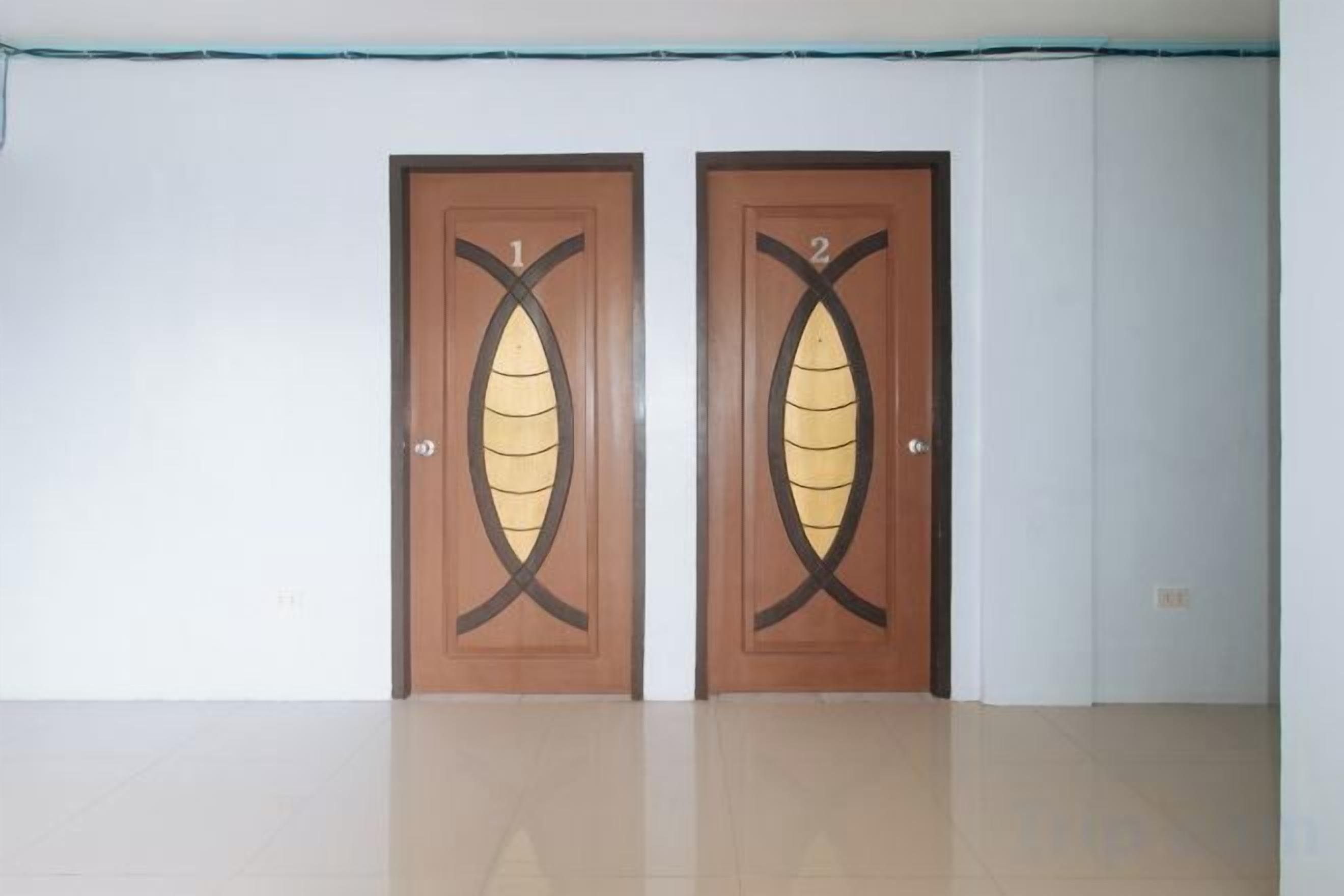 Two wooden doors with a leaf design, a white wall, and a tiled floor.