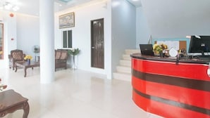 A hotel lobby with a reception desk, a staircase, and a seating area with chairs and a table.