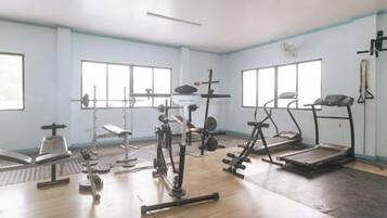 A gym with various exercise equipment, large windows, and a wooden floor.