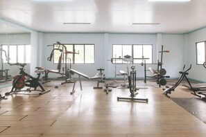 A gym with various exercise equipment, large windows, and a wooden floor.