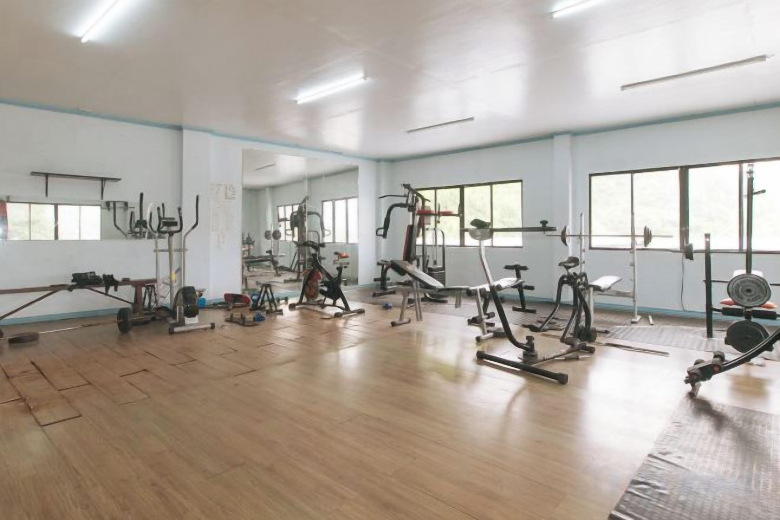 Une salle de sport équipée de divers appareils d’exercice, dotée de grandes fenêtres et d’un plancher en bois.