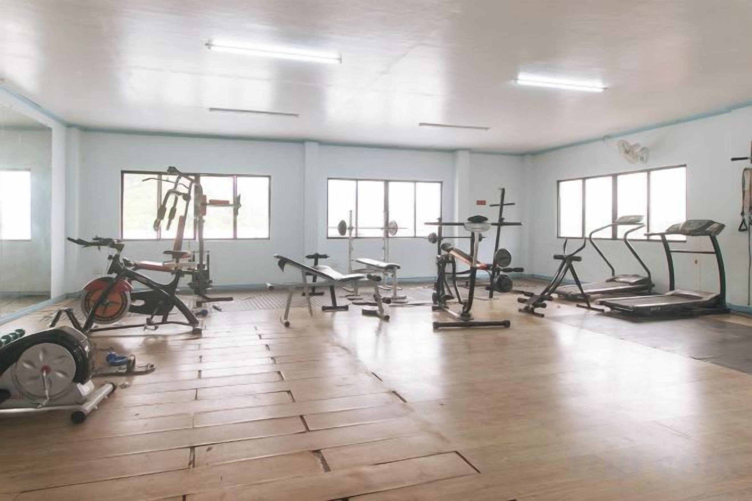 A gym with various exercise equipment, large windows, and a wooden floor.