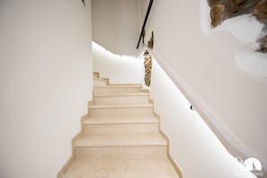 A staircase with beige steps leading upwards, white walls, and a stone accent wall. - Residenza Elena - Appartamento Mille Miglia (Moniga del Garda)