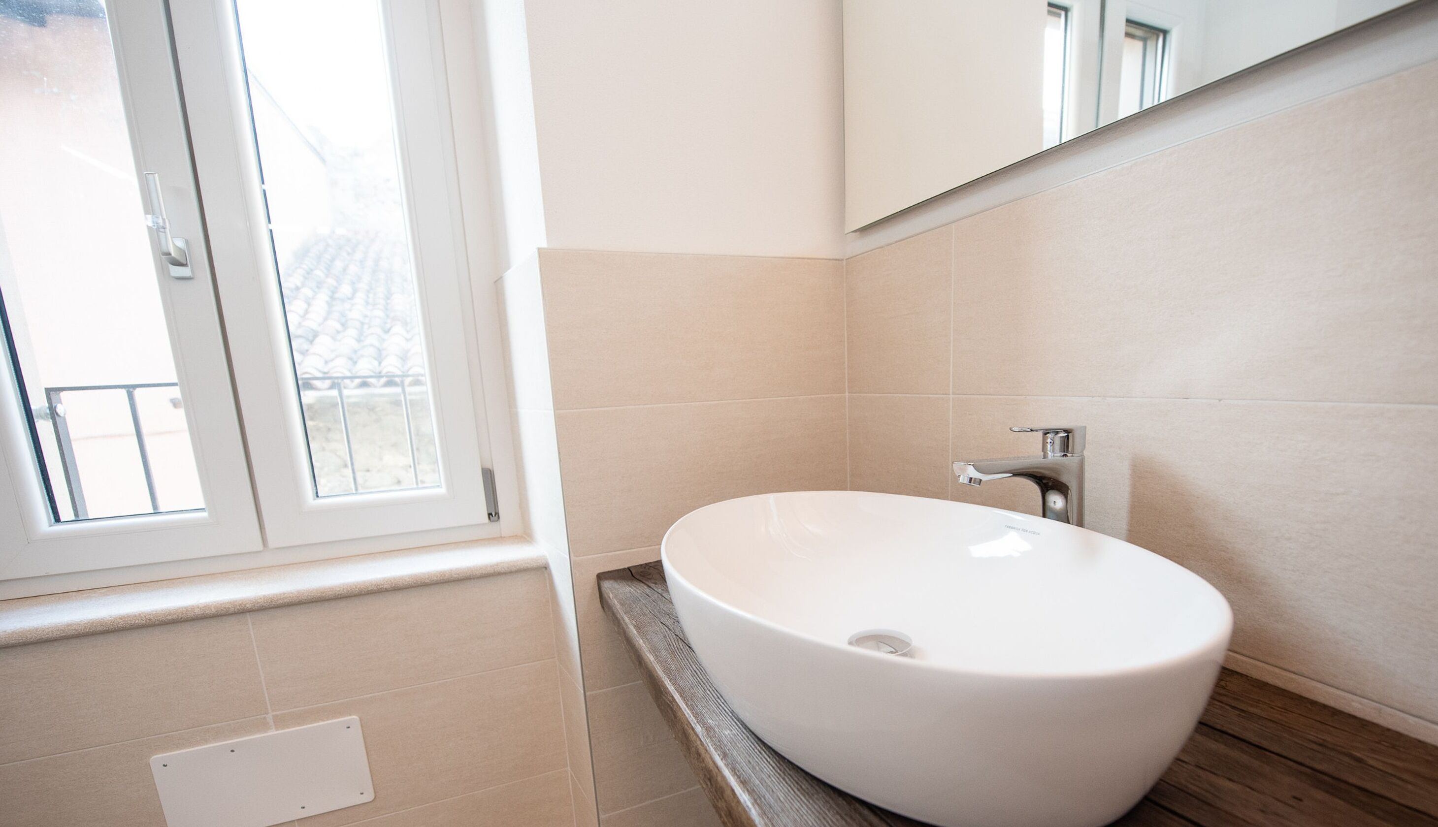Un baño con un lavabo blanco, un espejo y una ventana.