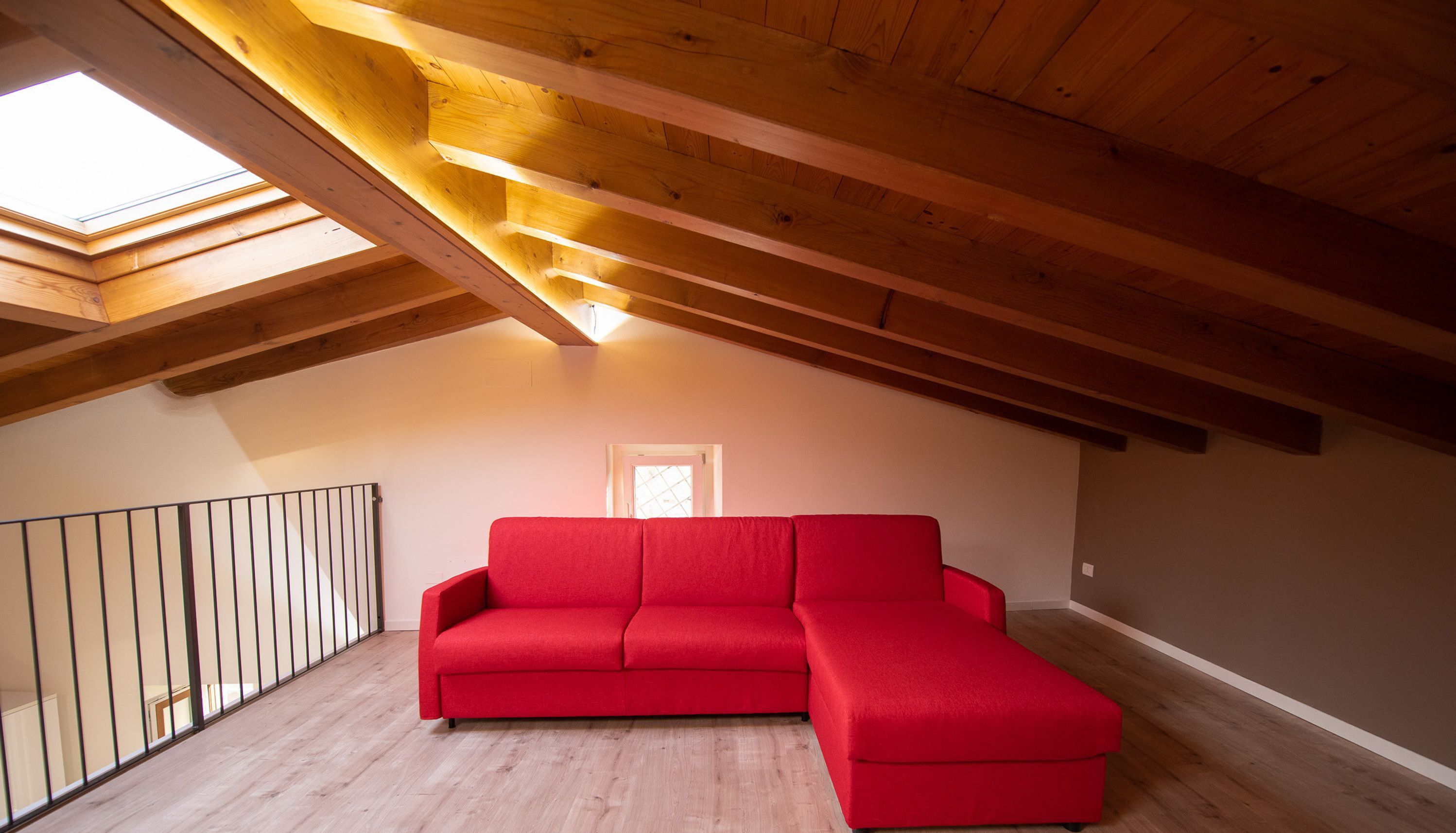 Un sofá seccional rojo en un dormitorio estilo loft con vigas de madera y tragaluces.