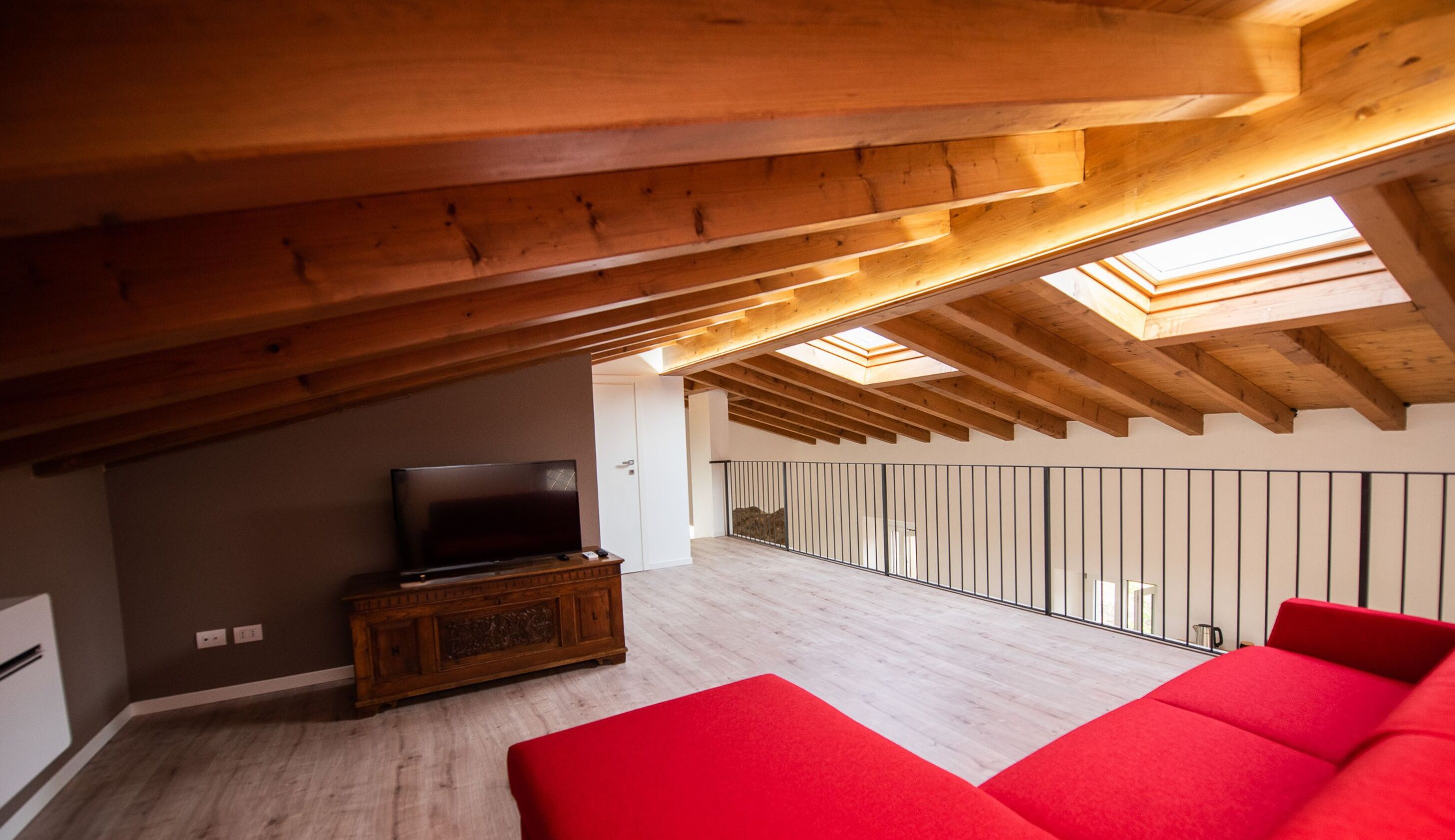 A spacious attic room with a wooden ceiling, a television on a cabinet, and a red sofa.