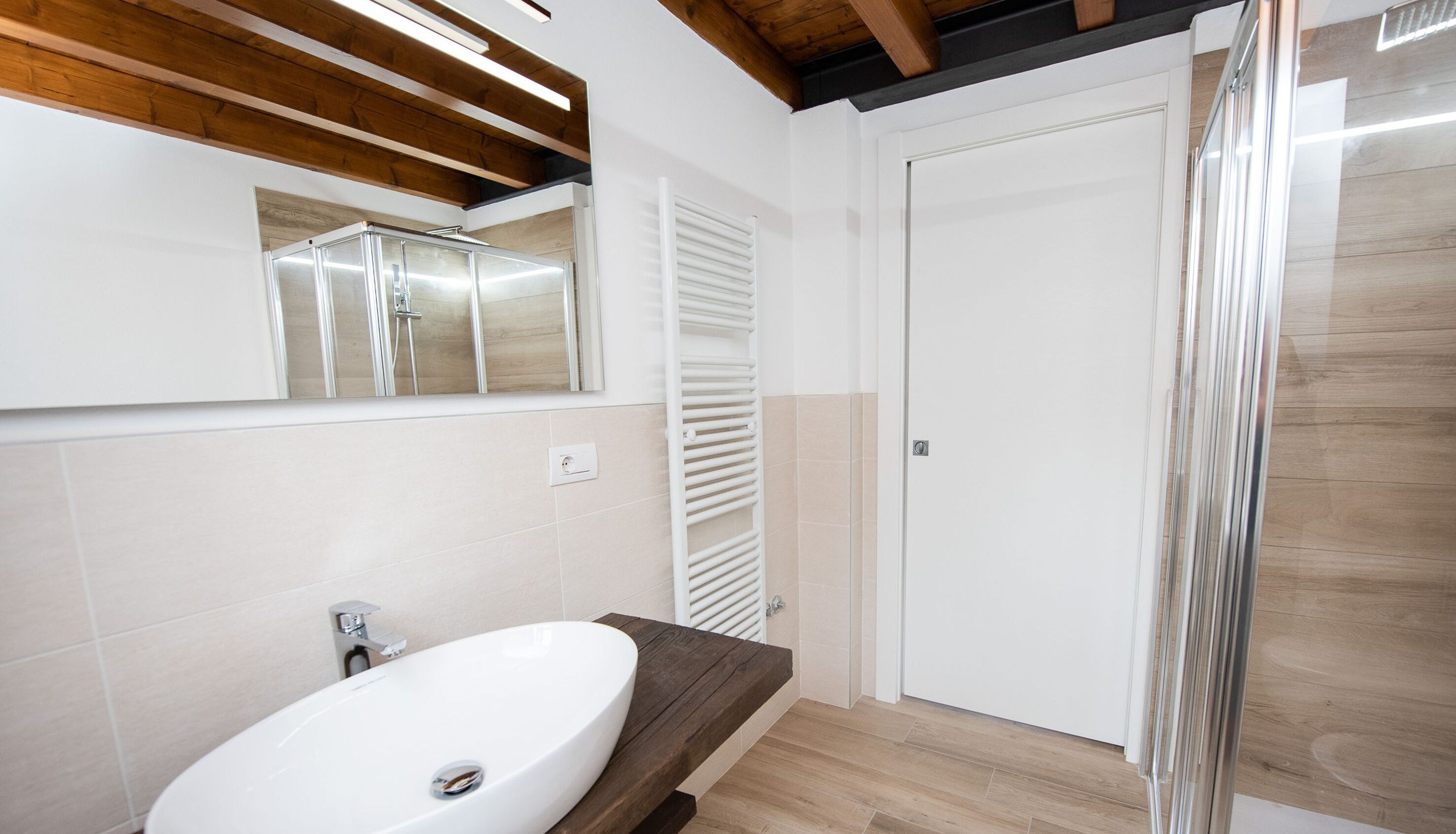Un bagno moderno con un lavandino bianco, un piano d'appoggio in legno e uno specchio grande.
