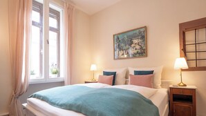 A bedroom with a large bed, two bedside tables with lamps, a window with curtains, and a painting on the wall. - Schmuckstück Maikammer - extraordinary apartments in the heart of Maikammer Whg. 1 (Maikammer)