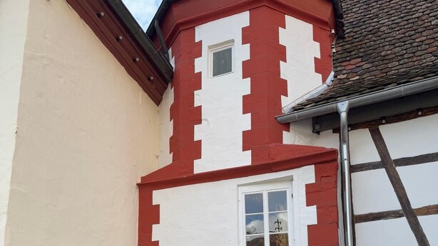 A building with a white and red facade, a small window, and a staircase leading to an entrance. - Schmuckstück Maikammer - extraordinary apartments in the heart of Maikammer Whg. 1 (Maikammer)