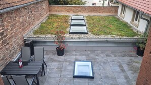 A rooftop patio with a garden, a table with chairs, and a glass door. - Schmuckstück Maikammer - extraordinary apartments in the heart of Maikammer Whg. 1 (Maikammer)