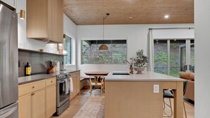 A modern kitchen with wooden cabinets, a stainless steel refrigerator, and a large island with a sink. - Modern home with 2 master bedrooms, private hot tub, garage and mountain views (Silver Star Mountain)