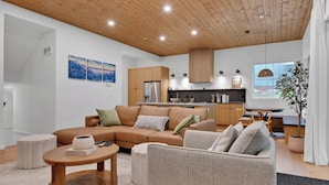 A modern living room with a sectional sofa, a round coffee table, and a kitchen in the background. - Modern home with 2 master bedrooms, private hot tub, garage and mountain views (Silver Star Mountain)