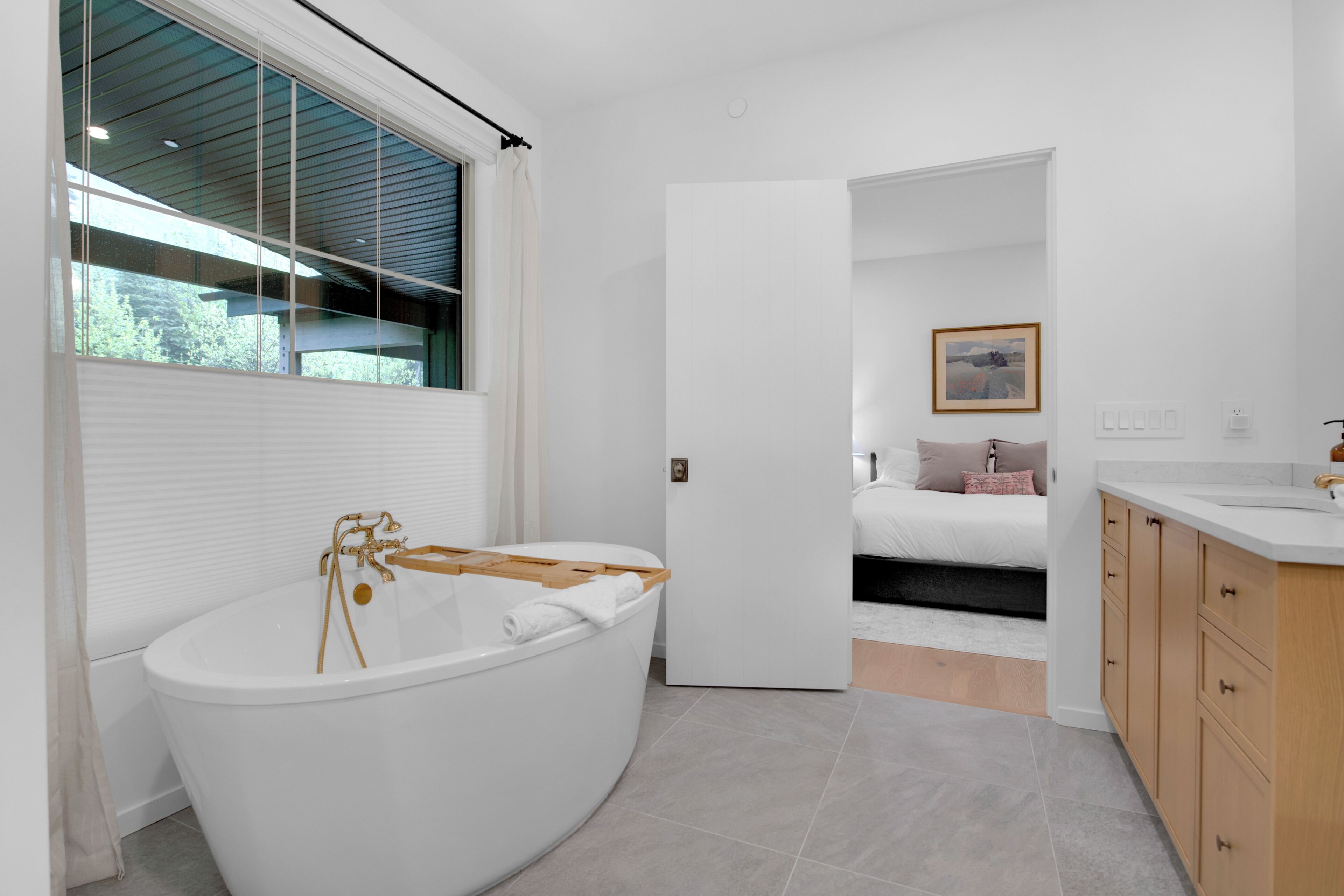 A modern bathroom with a freestanding bathtub, a wooden bath mat, and a large window.