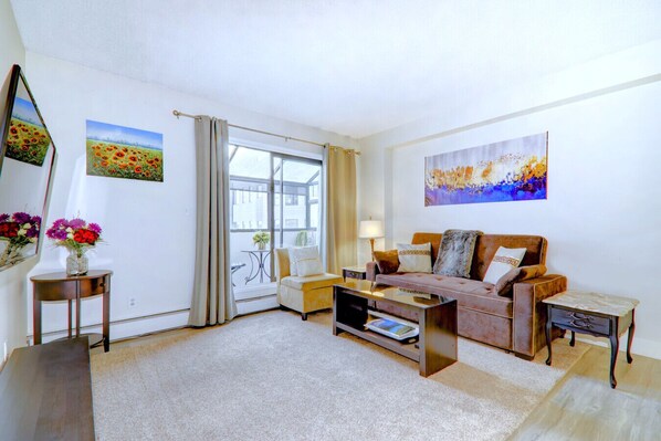 A living room with a sofa, a coffee table, a TV, and a small side table with a vase of flowers. - Spacious Top Floor at Stampede w/ Free Parking, AC (Calgary)