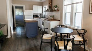Una cocina compacta con armarios blancos, una isla central y un comedor con cuatro sillas.