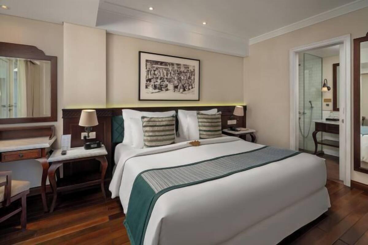 Hotelkamer met een groot bed, bureau, stoel, nachtkastje met lamp, een ingelijst schilderij aan de muur, en een deur naar de badkamer.