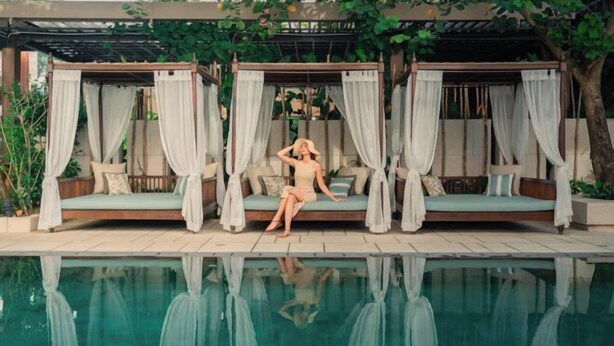 Un área junto a la piscina con una cama con dosel y una piscina cristalina.