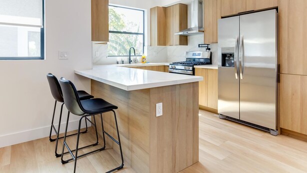 A modern kitchen with wooden cabinets, a stainless steel refrigerator, a gas stove, and a large window providing natural light. - Modern Luxe Retreat Three-Bedroom #4 (Los Angeles)