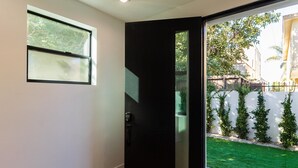 A modern entryway with a glass door leading to a green lawn and a white fence. - Modern Luxe Retreat Three-Bedroom #4 (Los Angeles)