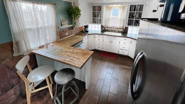 Una cocina con encimera de madera, armarios blancos y un refrigerador de acero inoxidable, además de un taburete de bar.