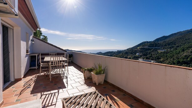 Una terraza en la azotea con mesa y sillas, plantas en macetas y vistas a un paisaje montañoso.