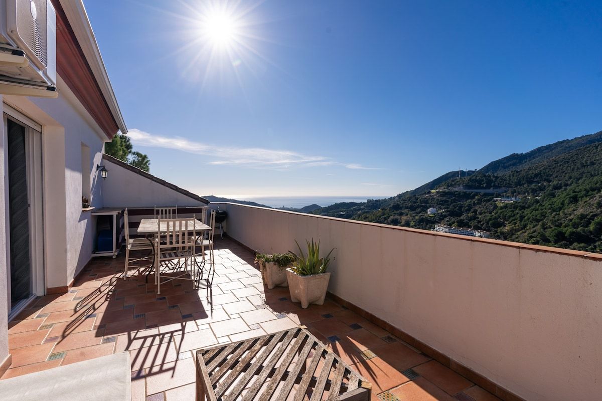 Terraza en la azotea con una mesa y sillas, plantas en macetas y vistas a un paisaje montañoso.