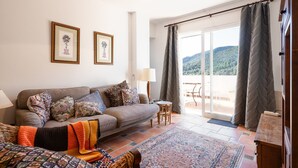 Una sala de estar acogedora con un sofá, cojines estampados, una mesita y vistas a un balcón con cortinas.