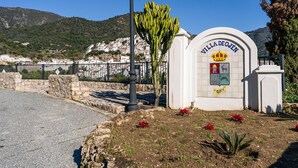Una villa llamada "Villa DeOijen" con fachada blanca, un emblema de corona y un cartel que indica un precio de 100€.