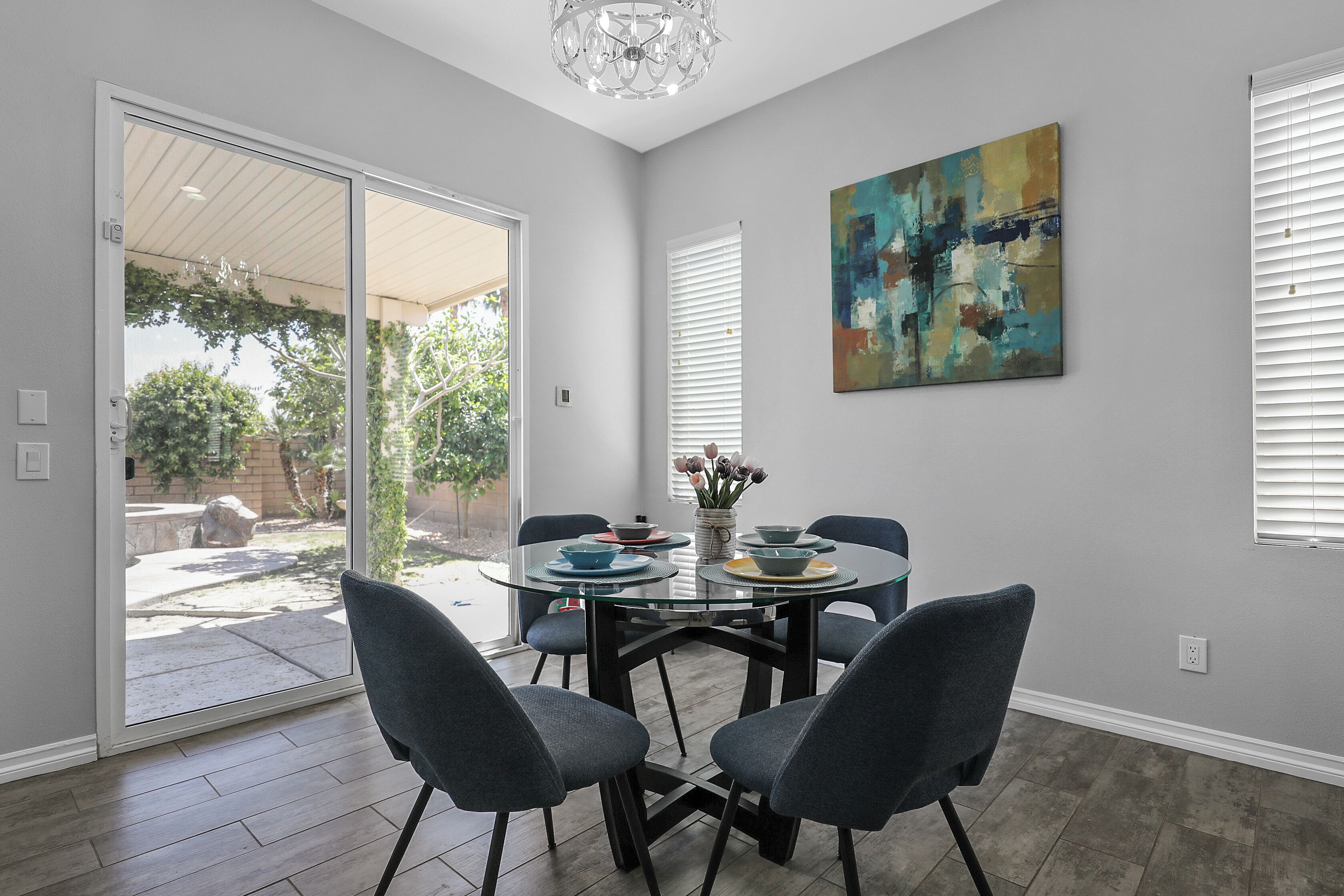 A dining area with a glass table, four chairs, and a vase with flowers.