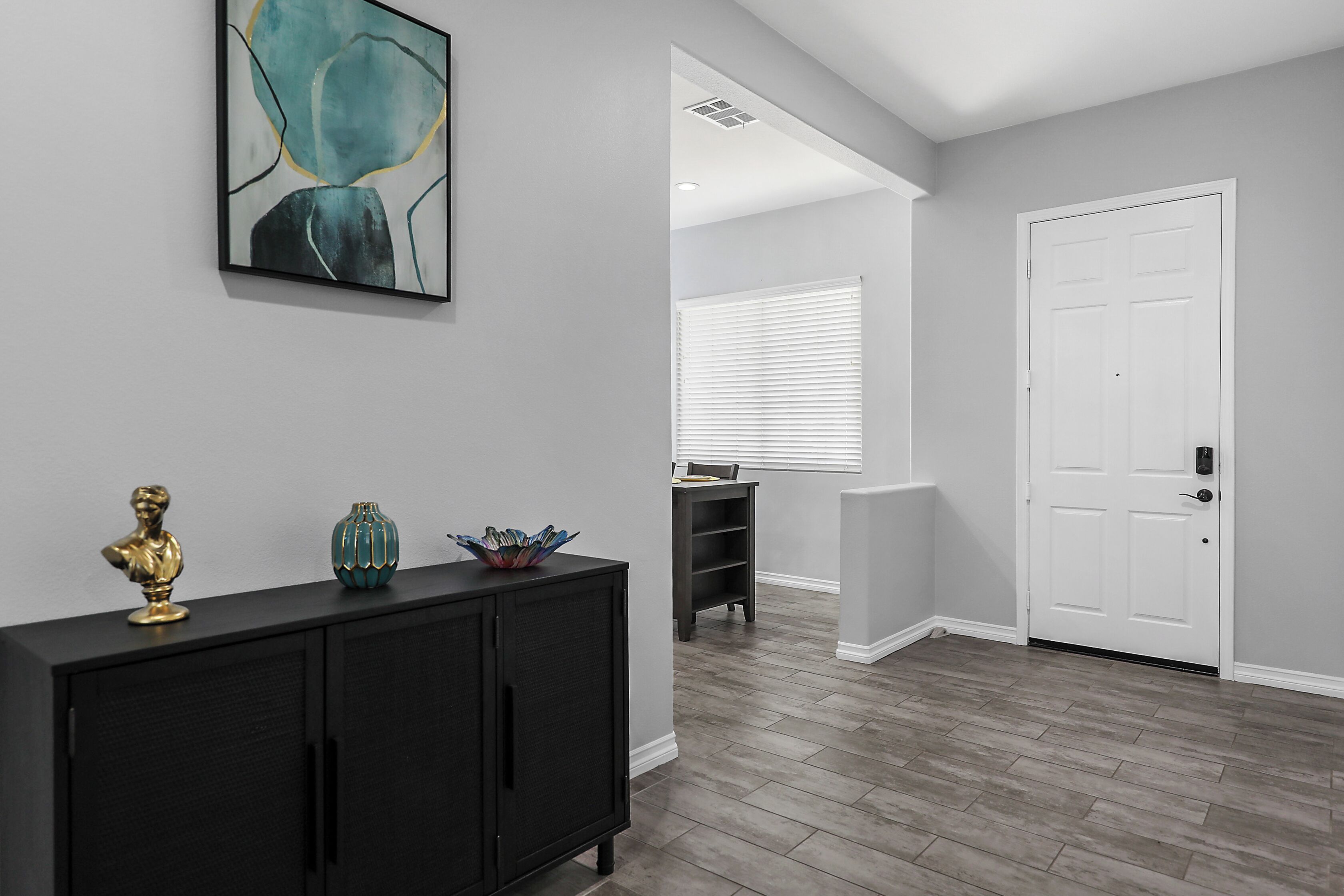 A hallway with a black console table, a white door, and a window with blinds.