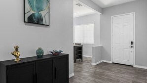 A hallway with a black console table, a white door, and a window with blinds. - Charming 4-bedroom house with private pool and spa in brilliant Indio (Indio)