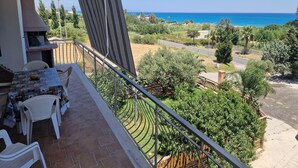 A balcony with a table and chairs, overlooking a coastal landscape with trees and a road.