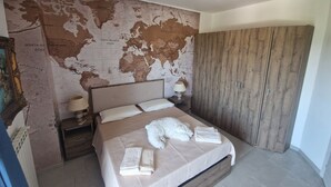 A bedroom with a large bed, a wooden wardrobe, a nightstand with a lamp, and a map on the wall.