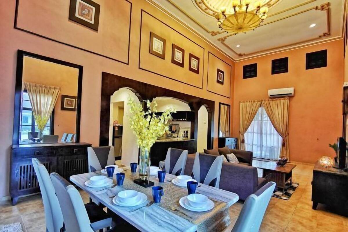 A dining area with a long table set for six, a sofa, and a chandelier.