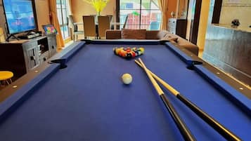 A pool table with balls and cues, a television, and a window with a view of buildings.