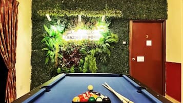A pool table with balls and cues, a door with a number, and a wall with a sign.