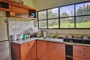A kitchen with a refrigerator, cabinets, a window, and a countertop with various kitchen items.