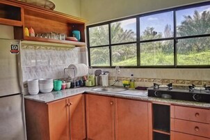 Una cocina con refrigerador, armarios, una ventana y una encimera con diversos utensilios de cocina.