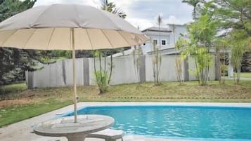 A swimming pool with a stone table and an umbrella.