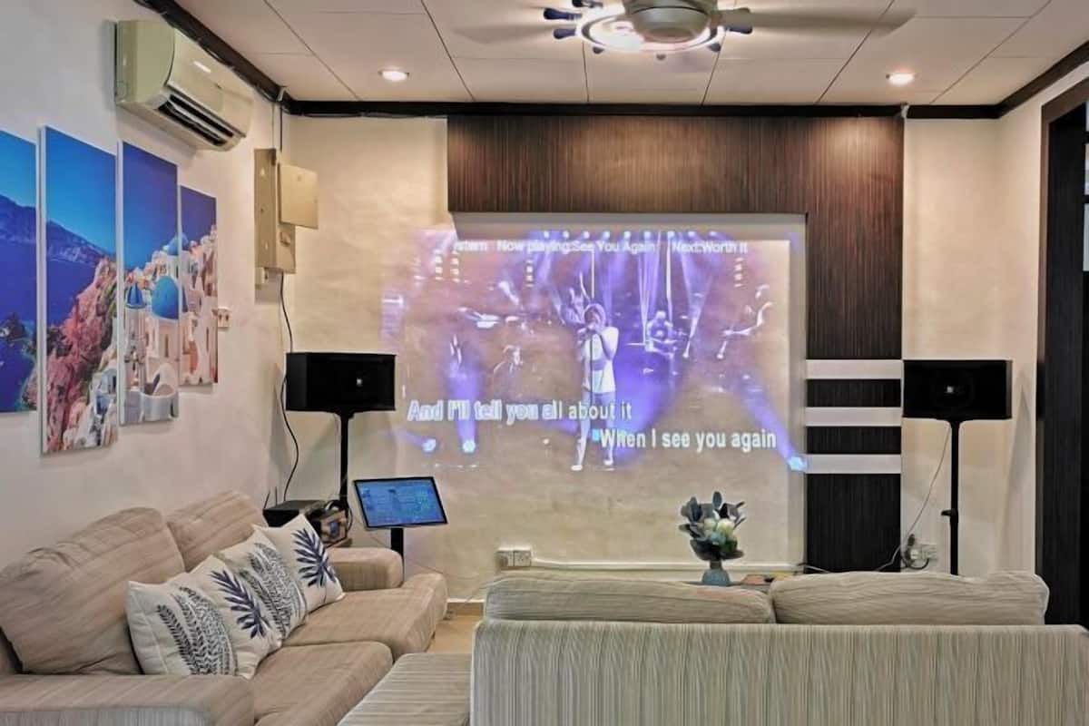 A modern hotel room with a large screen displaying a song, a sofa, a coffee table, and a wall-mounted air conditioner.