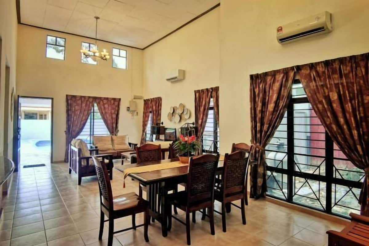 A dining area with a high ceiling, large windows with curtains, and a dining table set for six.